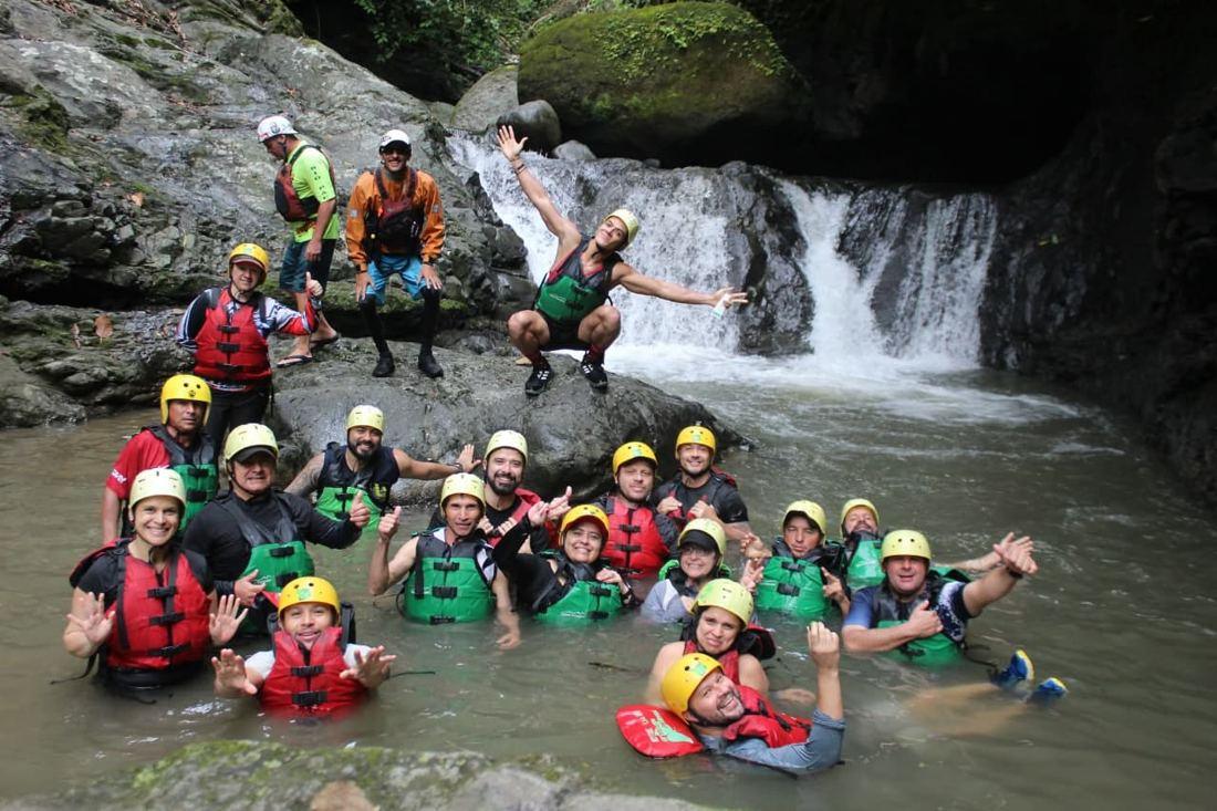 Grupo con chalecos y cascos en una poza bajo una catarata